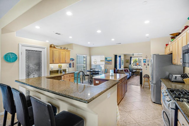 kitchen with appliances with stainless steel finishes, a kitchen breakfast bar, a large island, light tile patterned floors, and light brown cabinetry