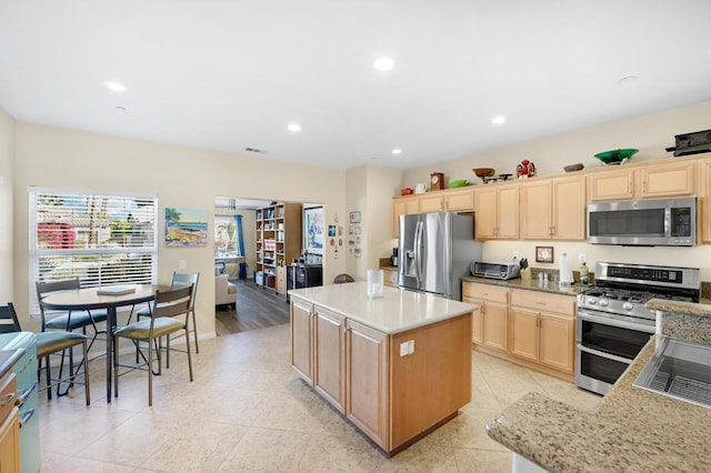 kitchen featuring a center island, light stone countertops, appliances with stainless steel finishes, light tile patterned floors, and light brown cabinetry