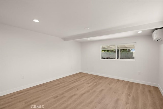 spare room featuring a wall mounted AC, beamed ceiling, and light hardwood / wood-style flooring