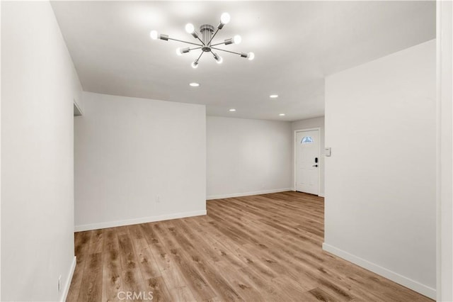 spare room with an inviting chandelier and light hardwood / wood-style floors