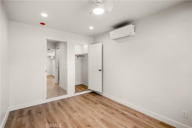 unfurnished bedroom featuring ceiling fan, a wall unit AC, and light wood-type flooring