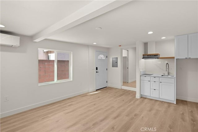 kitchen with white cabinetry, a wall unit AC, beam ceiling, light hardwood / wood-style flooring, and sink