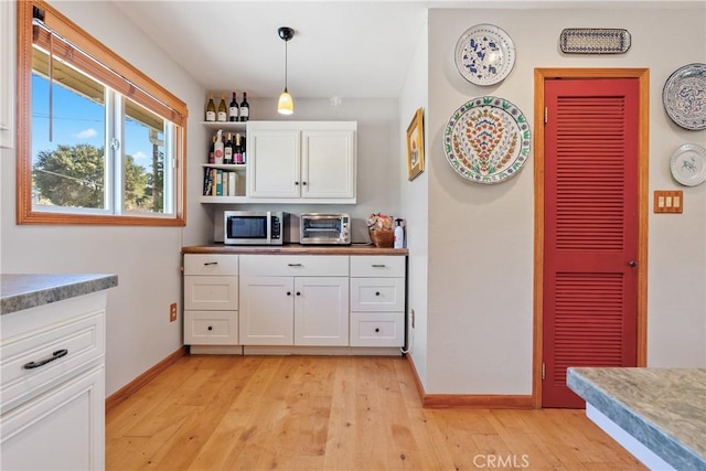 kitchen featuring hanging light fixtures, white cabinets, and light hardwood / wood-style flooring