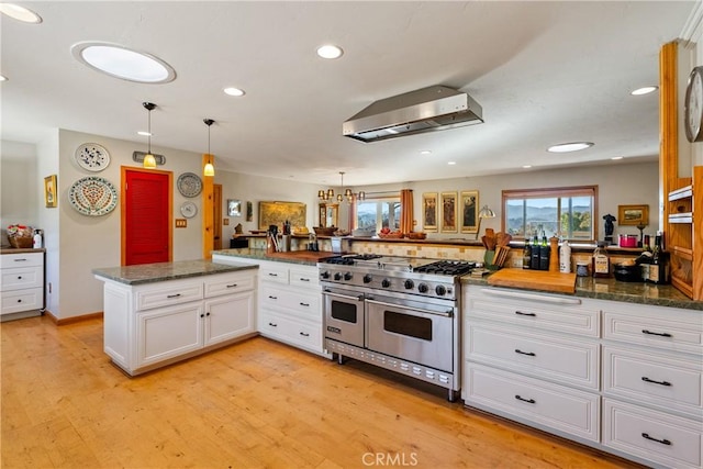 kitchen with double oven range, kitchen peninsula, hanging light fixtures, wall chimney range hood, and white cabinets