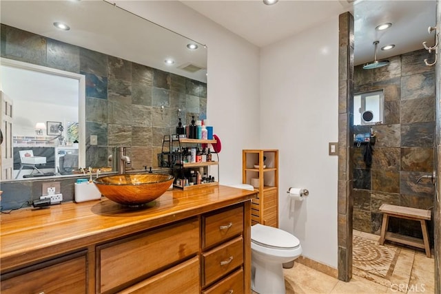 bathroom with toilet, a shower, tile walls, tile patterned floors, and vanity