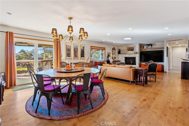 dining space with an inviting chandelier, light hardwood / wood-style flooring, and a stone fireplace