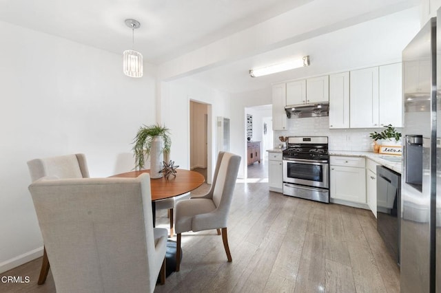 kitchen featuring white cabinets, decorative light fixtures, stainless steel appliances, decorative backsplash, and light wood-type flooring