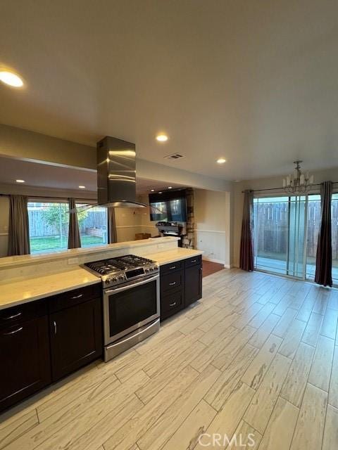 kitchen with wall chimney range hood, stainless steel range with gas cooktop, a chandelier, and light hardwood / wood-style floors