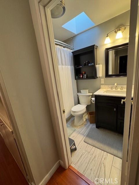 bathroom with wood-type flooring, vanity, a skylight, toilet, and walk in shower