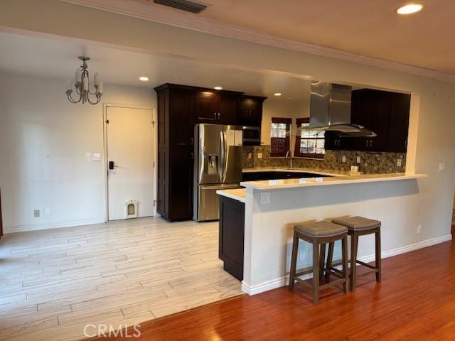 kitchen with extractor fan, kitchen peninsula, stainless steel refrigerator with ice dispenser, decorative backsplash, and an inviting chandelier