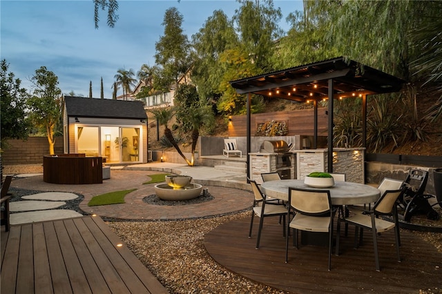 patio terrace at dusk with a shed, exterior kitchen, a deck, and a grill