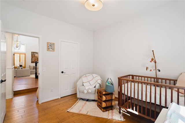 bedroom featuring an inviting chandelier, wood-type flooring, and a nursery area