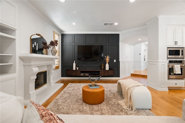 living room featuring crown molding, built in features, and light hardwood / wood-style flooring