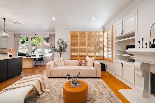 living room featuring built in shelves, ornamental molding, a notable chandelier, and light wood-type flooring