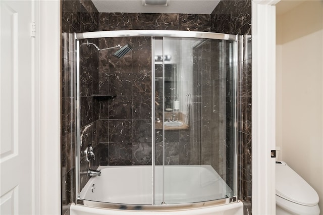 bathroom featuring toilet, bath / shower combo with glass door, and a textured ceiling