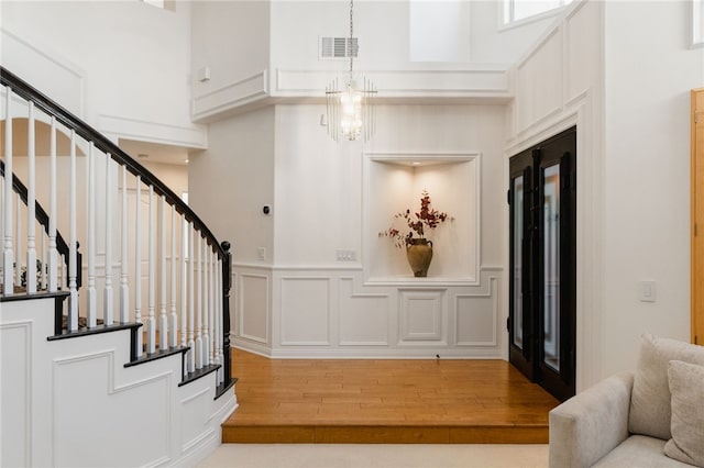 entrance foyer featuring french doors, a towering ceiling, a notable chandelier, and light hardwood / wood-style floors