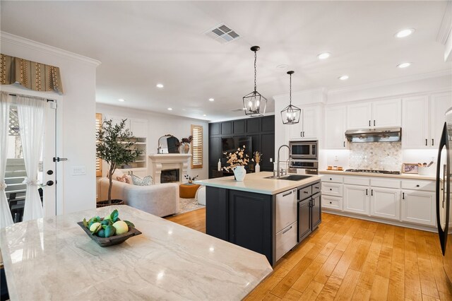 kitchen with hanging light fixtures, white cabinets, appliances with stainless steel finishes, and a center island with sink