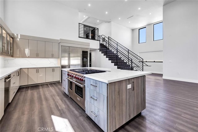 kitchen featuring double oven range, decorative backsplash, dark wood-type flooring, a towering ceiling, and light stone countertops