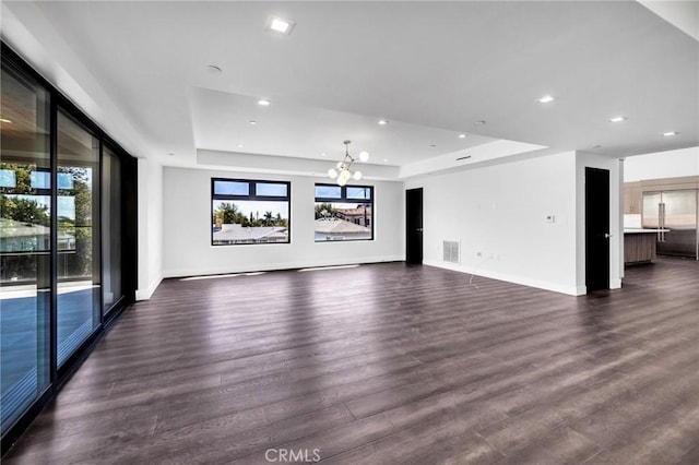 unfurnished living room featuring dark hardwood / wood-style floors, a raised ceiling, and an inviting chandelier