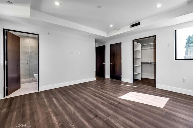 unfurnished bedroom with dark wood-type flooring, a spacious closet, connected bathroom, and a raised ceiling