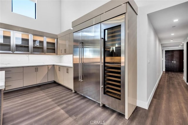 kitchen with light stone counters, backsplash, stainless steel built in fridge, and dark hardwood / wood-style floors