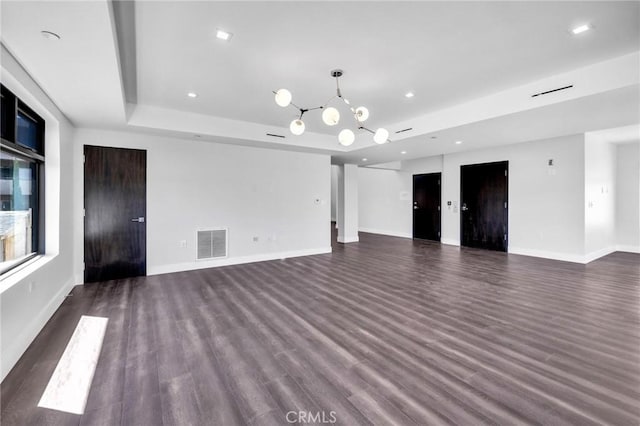 unfurnished living room featuring dark wood-type flooring, a raised ceiling, and a notable chandelier