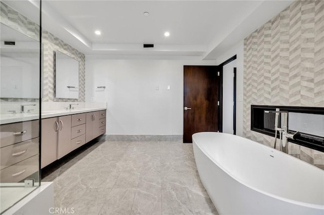 bathroom with a raised ceiling, vanity, and a bathtub