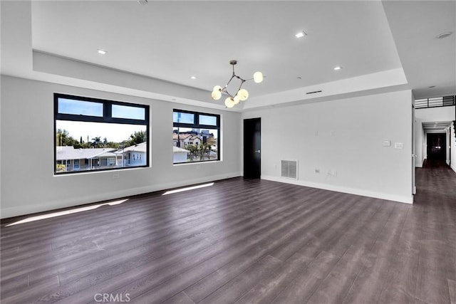 unfurnished living room featuring an inviting chandelier, dark hardwood / wood-style flooring, and a raised ceiling