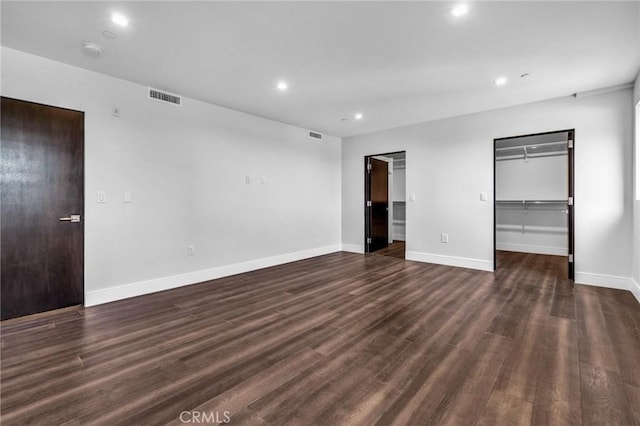 unfurnished bedroom featuring a spacious closet, dark wood-type flooring, and a closet