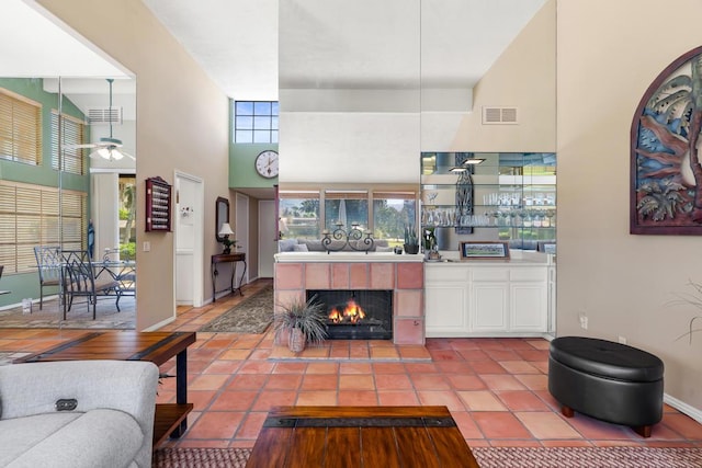 living room featuring ceiling fan, a high ceiling, a tile fireplace, and a healthy amount of sunlight