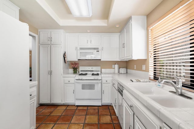 kitchen with white appliances, white cabinets, sink, tile countertops, and a tray ceiling