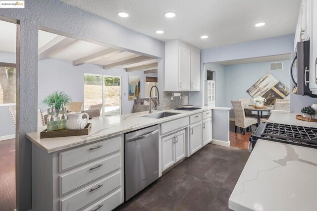 kitchen with light stone countertops, appliances with stainless steel finishes, white cabinetry, sink, and beam ceiling