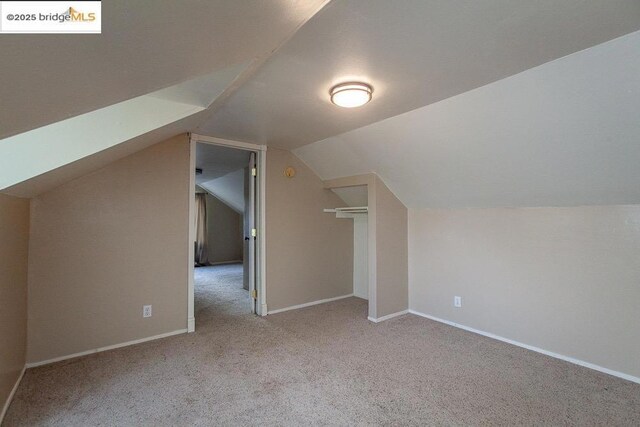 additional living space featuring vaulted ceiling and light colored carpet