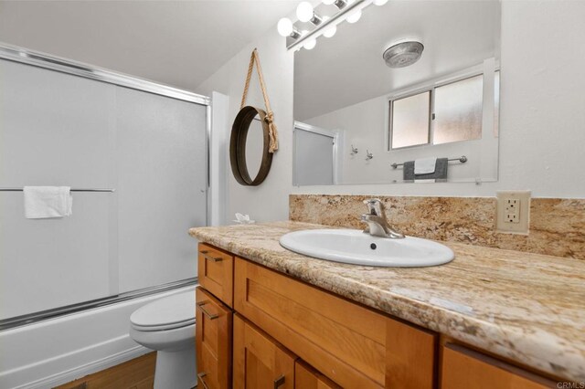 full bathroom with vanity, hardwood / wood-style flooring, bath / shower combo with glass door, and toilet