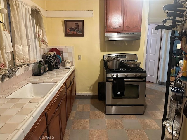 kitchen with stainless steel gas range, tile countertops, and sink