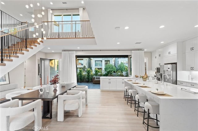 kitchen featuring white cabinets, decorative light fixtures, a kitchen breakfast bar, stainless steel fridge, and light wood-type flooring