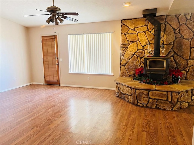 unfurnished living room featuring ceiling fan, a wood stove, and wood-type flooring