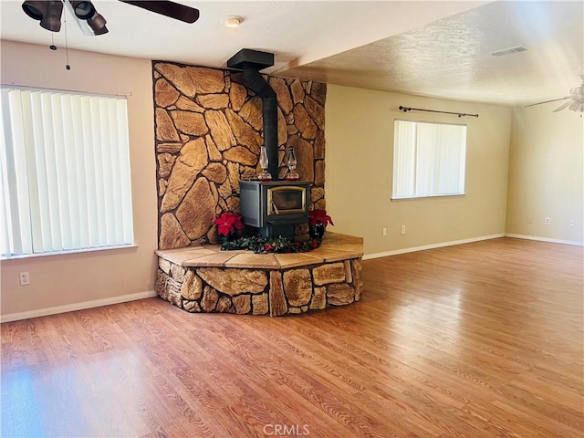 unfurnished living room featuring a wood stove, hardwood / wood-style floors, a wealth of natural light, and a textured ceiling