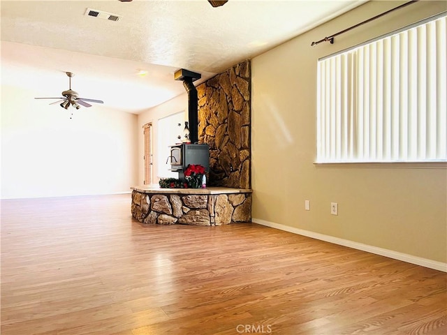 living room featuring light hardwood / wood-style floors, a wood stove, and ceiling fan