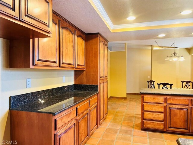 kitchen featuring light tile patterned floors, a tray ceiling, a chandelier, dark stone counters, and ornamental molding