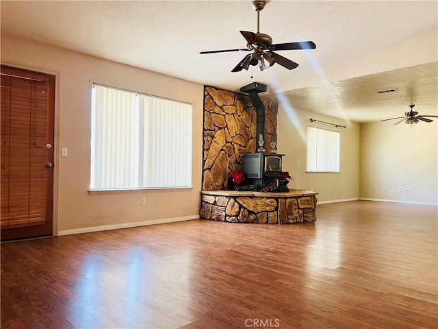 living room with ceiling fan, a wood stove, and wood-type flooring