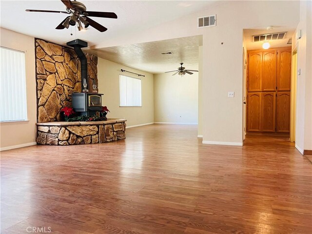 unfurnished living room featuring ceiling fan, a wood stove, and hardwood / wood-style floors