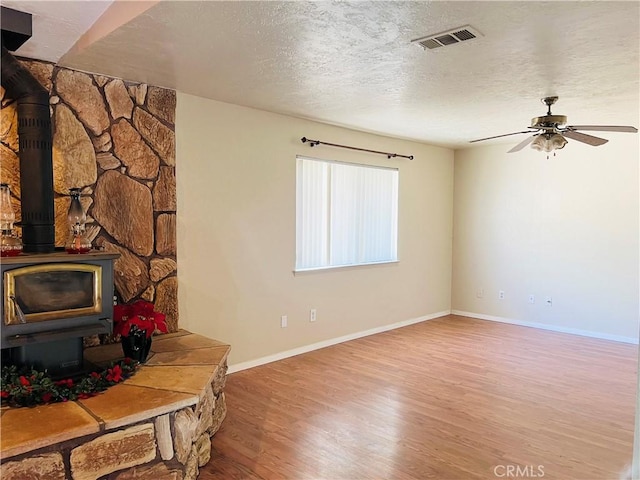 unfurnished living room featuring ceiling fan, wood-type flooring, a wood stove, and a textured ceiling