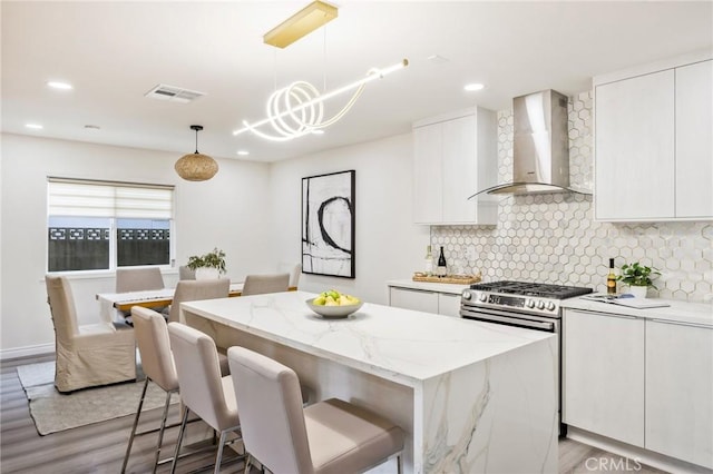 kitchen with white cabinetry, wall chimney exhaust hood, pendant lighting, and a kitchen island