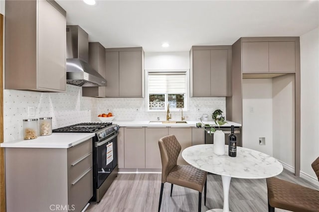 kitchen featuring stainless steel gas stove, sink, wall chimney exhaust hood, and gray cabinets