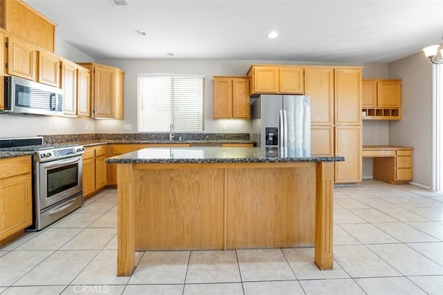 kitchen featuring light tile patterned flooring, appliances with stainless steel finishes, dark stone counters, and a center island