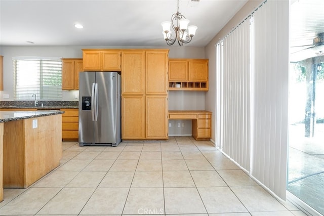 kitchen featuring an inviting chandelier, stainless steel fridge, decorative light fixtures, dark stone countertops, and sink