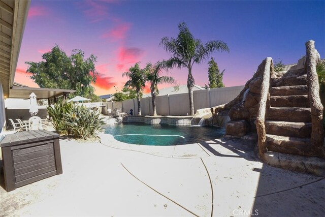 pool at dusk featuring pool water feature and a patio