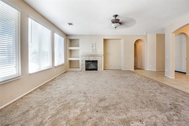 unfurnished living room with ceiling fan, light colored carpet, built in shelves, and a fireplace