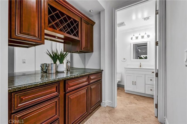 bar featuring light tile patterned floors, dark stone counters, and sink